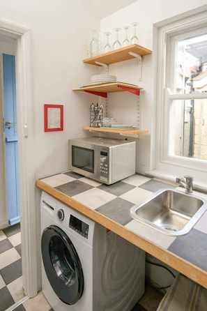 Une cuisine compacte équipée d’un lave-linge, d’un four à micro-ondes, d’un évier et d’étagères pour ranger la vaisselle.