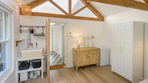 A room with a wooden ceiling, a white wardrobe, a wooden cabinet, and a window with a view of buildings.