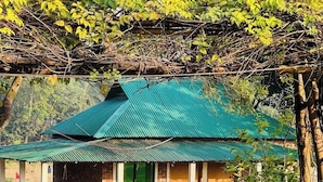 A single-story building with a green metal roof, brick walls, and a small porch area with seating. - Reverie Resort (Gazipur)
