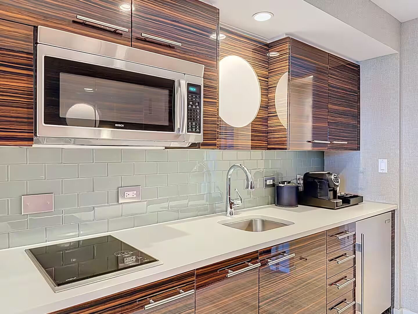 A modern kitchen with a Bosch microwave, a built-in induction cooktop, a sink, and wooden cabinetry.