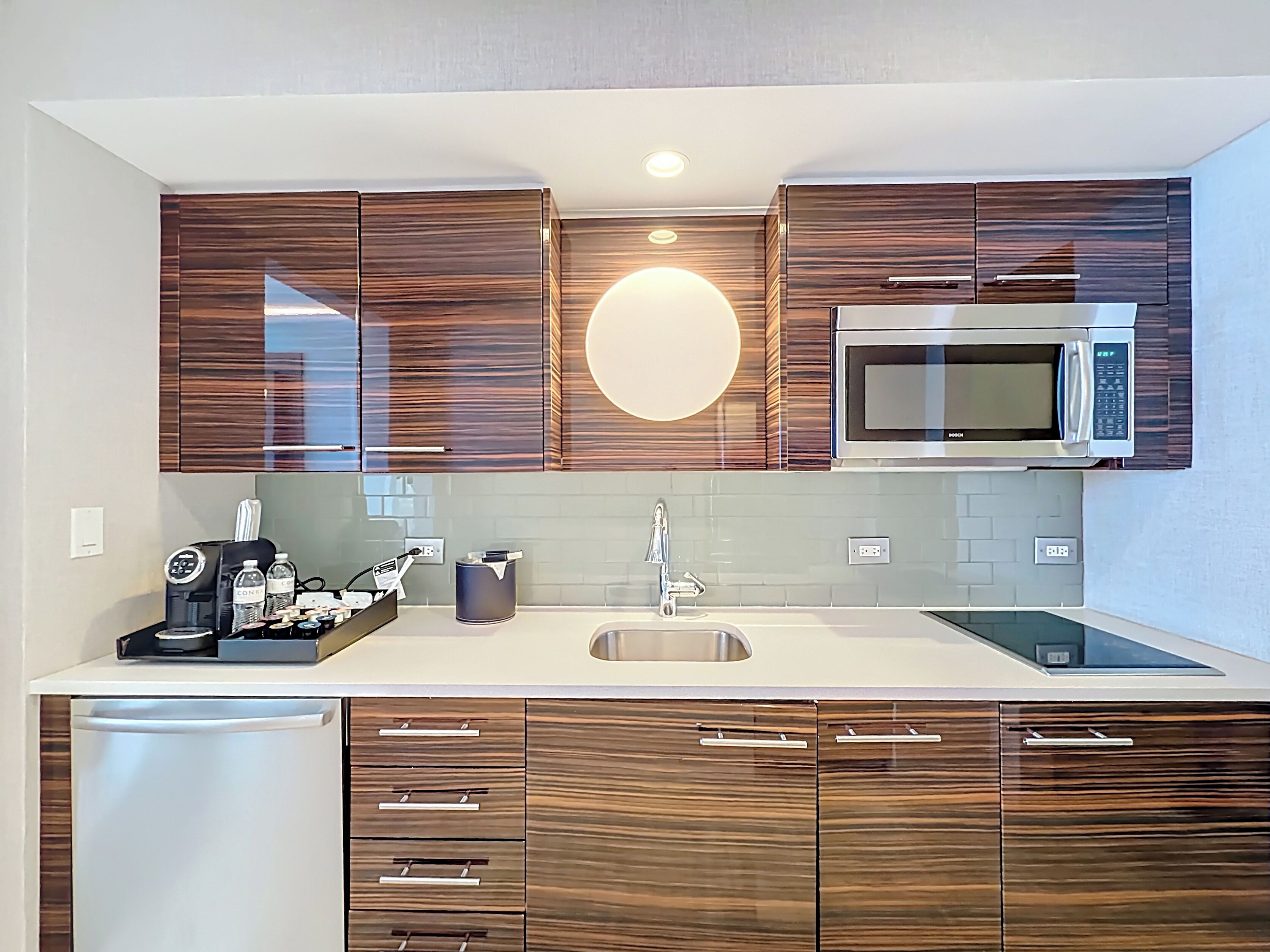 A modern kitchen with wooden cabinets, a built-in microwave, a coffee machine, and a sink.