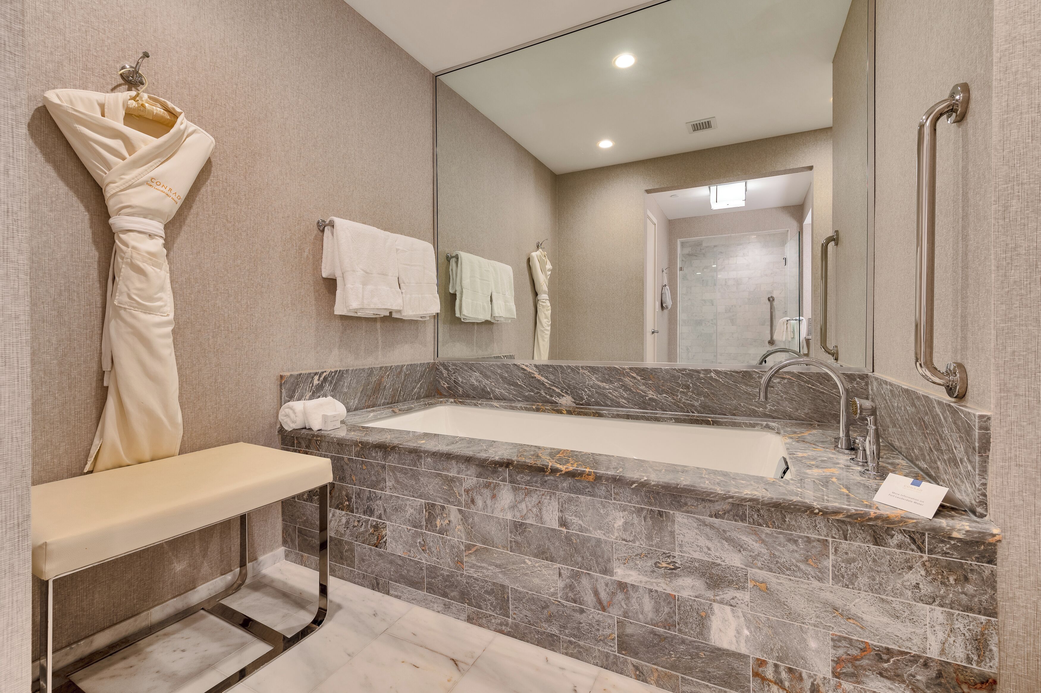Un baño moderno con un lavabo de mármol, un banco y un espejo grande.
