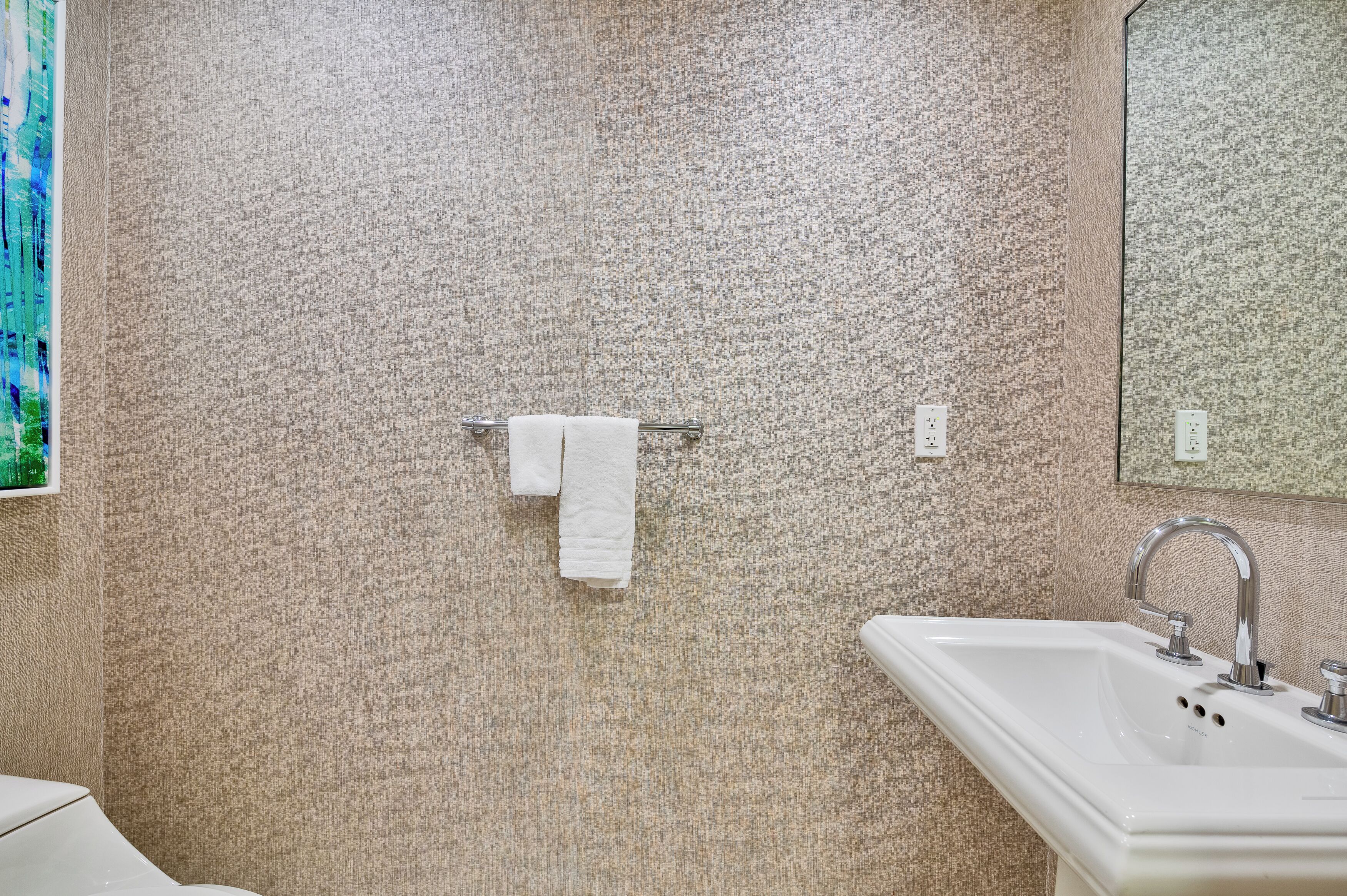 Een badkamer met een lichtbeige muur met structuur, een wit wastafelmeubel met chromefaucet en een handdoek aan een metalen handdoekhouder.