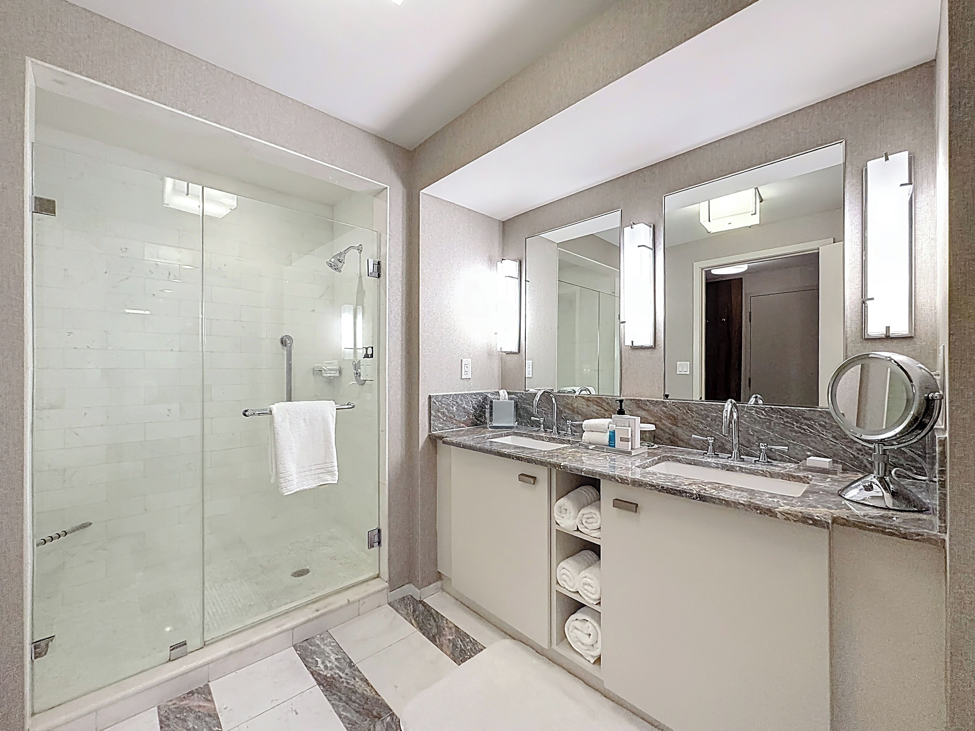 A modern bathroom with a glass-enclosed shower, a vanity with a marble countertop, and a large mirror.