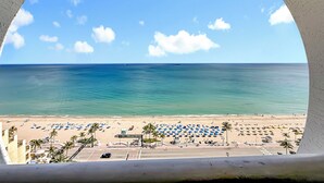 A beach view through a circular window, featuring a sandy beach, palm trees, and a clear blue sky. - Luxury Suites at Fort Lauderdale Beach (Fort Lauderdale)