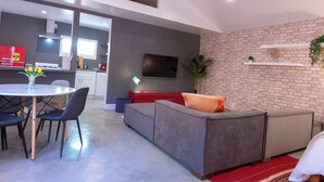 Ein modernes Wohnzimmer mit Essbereich, grauem Sofa, roter Akzentwand und einem flachbildfernseher, der an der Ziegelwand angebracht ist.