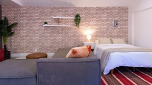 Ein modernes Schlafzimmer mit Backsteinwand, einem Bett, einer Couch, einem Nachttisch und einer Pflanze.