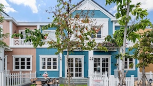 Una casa de dos pisos con fachada azul y rosa, ventanas blancas y cerca de piquete blanca.