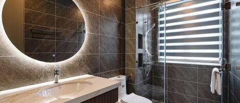 A modern bathroom with a marble vanity, a toilet, a glass shower enclosure, and a large mirror.
