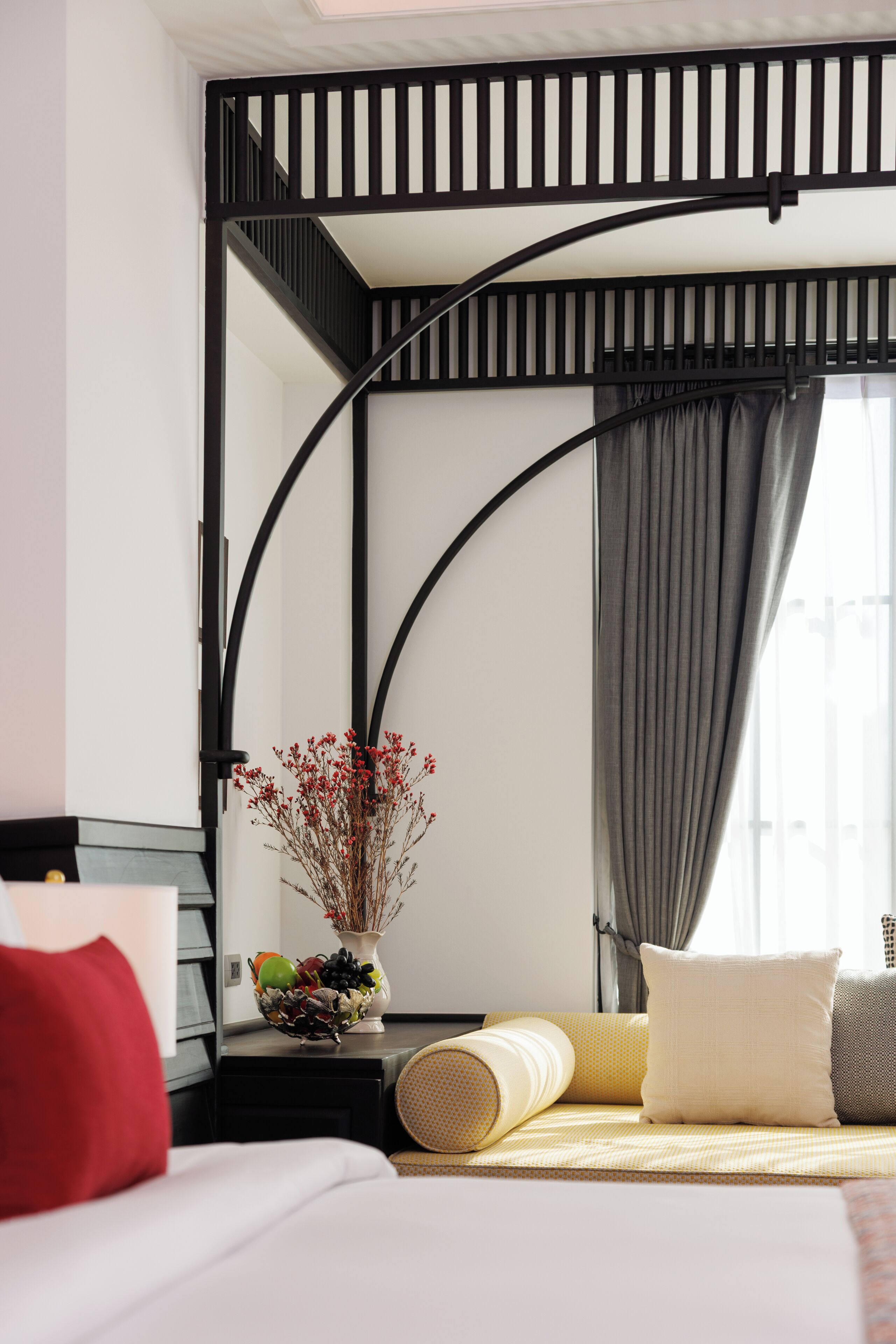 A modern hotel room with a bed, a nightstand with a vase of flowers, and a window with curtains.