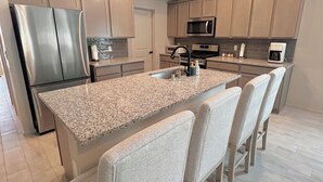 A modern kitchen with a large island, stainless steel appliances, and a herringbone-patterned backsplash. - The paradise house in Roswell (Roswell)