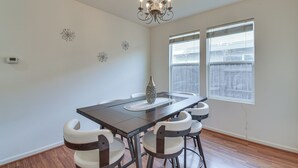 A dining area with a dark wooden table, white chairs, a chandelier, and decorative wall art. - 7 Mi to Lake Yosemite: Family Home w/ Fenced Yard (Merced)