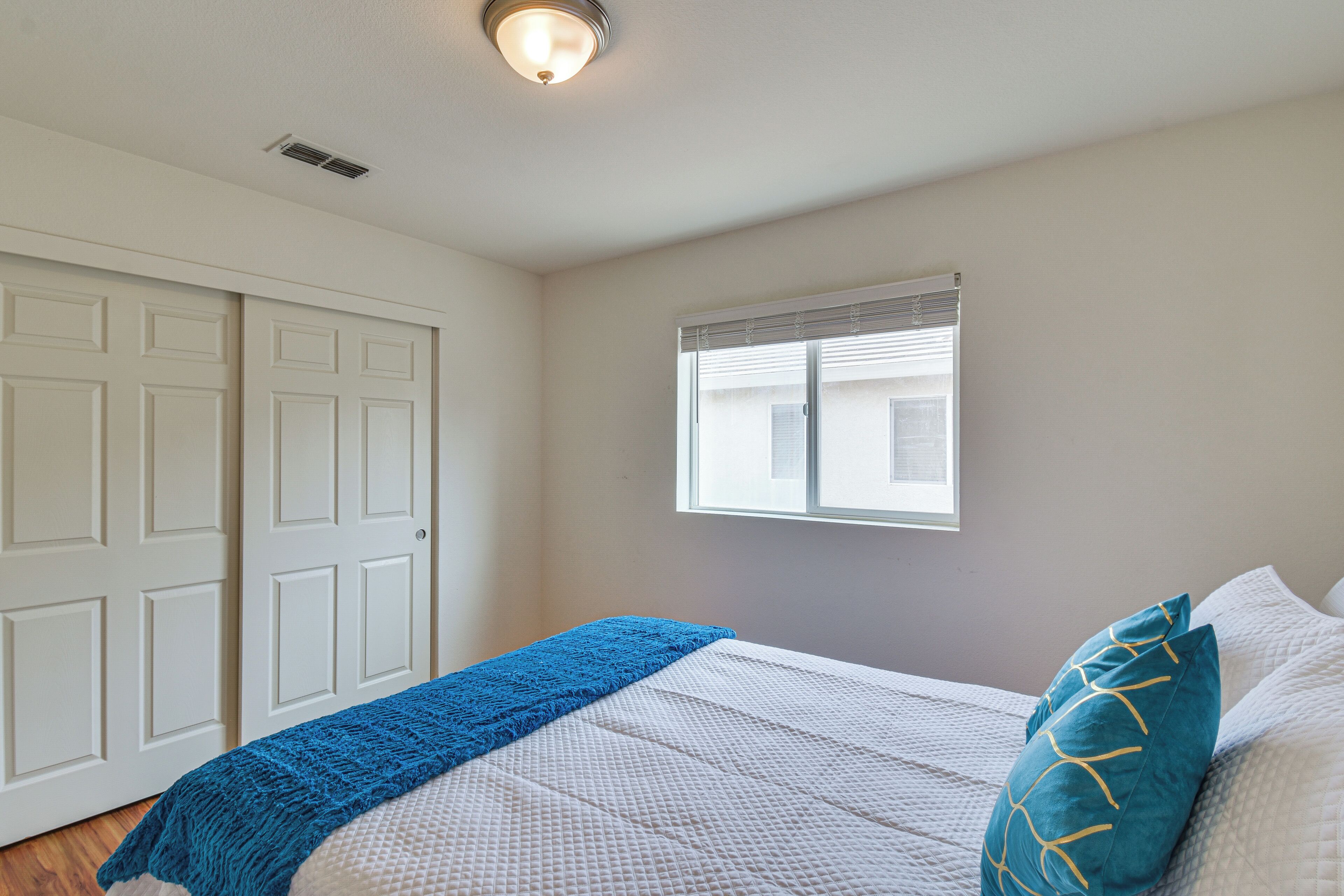 Une chambre à coucher avec un lit, une fenêtre avec des stores, une porte et un luminaire au plafond.