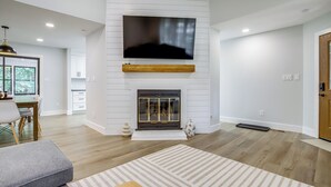 Een moderne woonkamer met een open haard, een flatscreen televisie erboven en een eethoek met een tafel en stoelen.