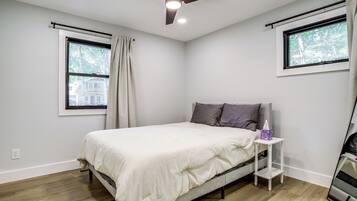 A bedroom with a bed, a ceiling fan, a window with curtains, and a bedside table with a tissue box.