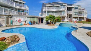 Une piscine au design incurvé, entourée d’un bâtiment doté de nombreux balcons et d’un petit jardin.