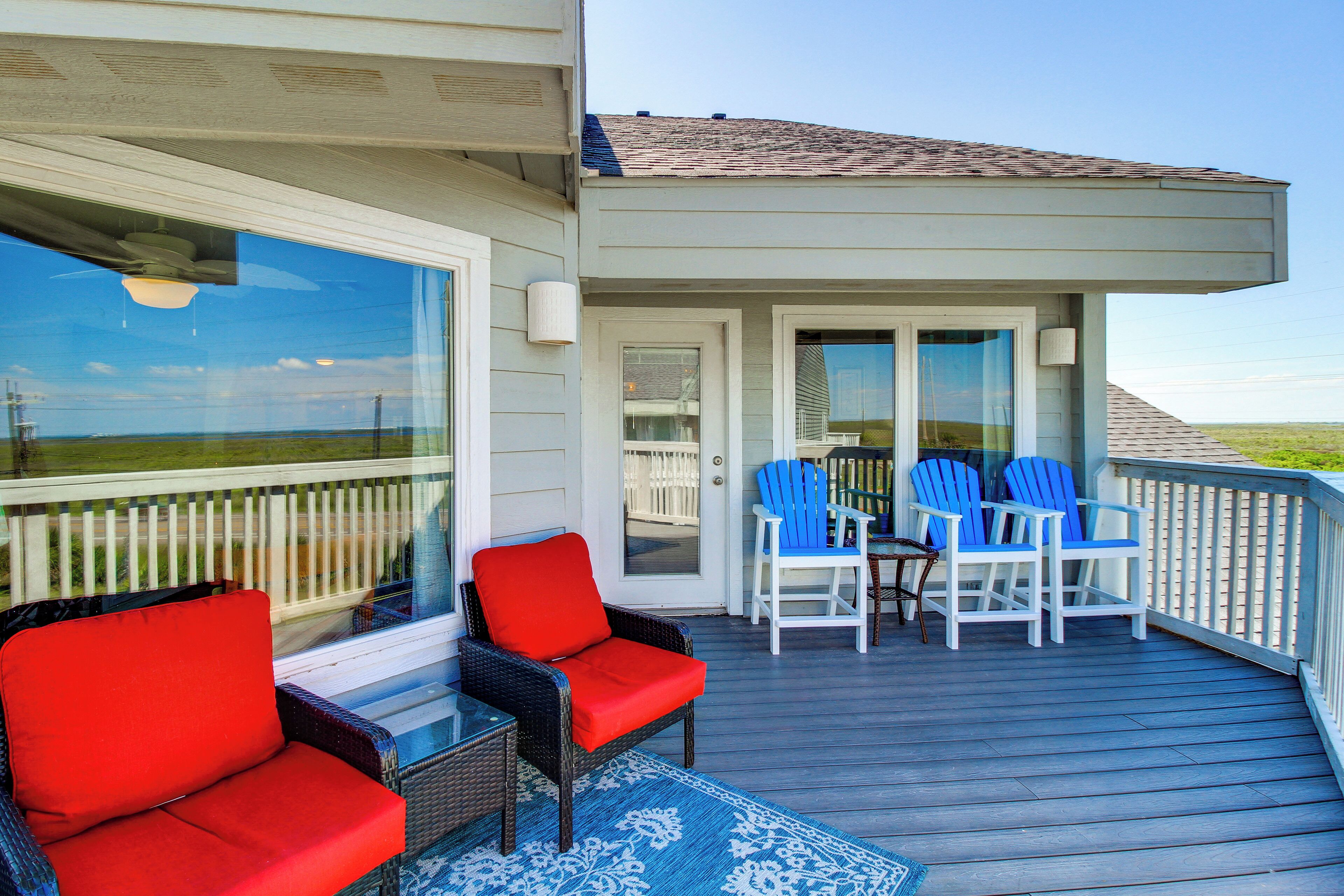 A covered outdoor deck with wicker chairs and a table, a glass door leading to a covered porch, and a view of the landscape.