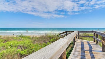 A wooden boardwalk leading to a beach with a clear sky and ocean view.