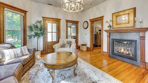 A spacious living room with hardwood floors, a fireplace, a large chandelier, and a comfortable seating area. - Downtown Walkability - 'The Purple House' (Berthoud)