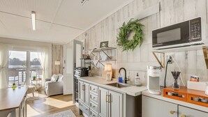 A modern kitchen with a built-in microwave, a coffee maker, and a sink. There is a dining area with a table and chairs, and a view of the outdoors through large windows. - Cozy Cottage on Main Channel of Lay Lake (Wilsonville)