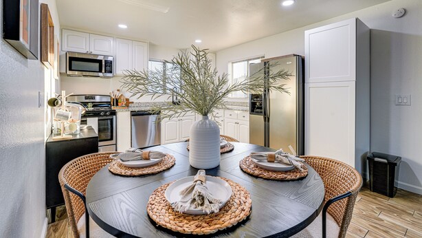 A modern kitchen with white cabinets, a microwave, and a refrigerator. There is a dining table with placemats and a vase with branches. - Easy Walk to Dtwn Gilbert, Family-Friendly Oasis! (Gilbert)