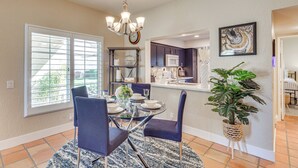 A dining area with a round table, chairs, a chandelier, a potted plant, and a view of the kitchen. - Golf Course View & Pool Access: Palm Desert Condo (Palm Desert)
