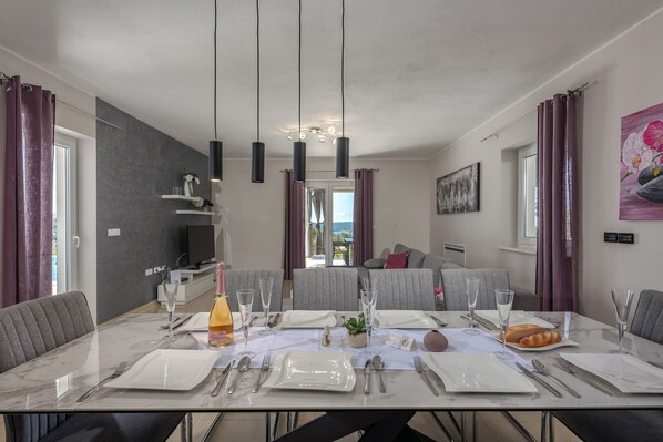 A dining area with a marble table set for six, featuring a bottle of orange juice, a small plant, and a croissant.
