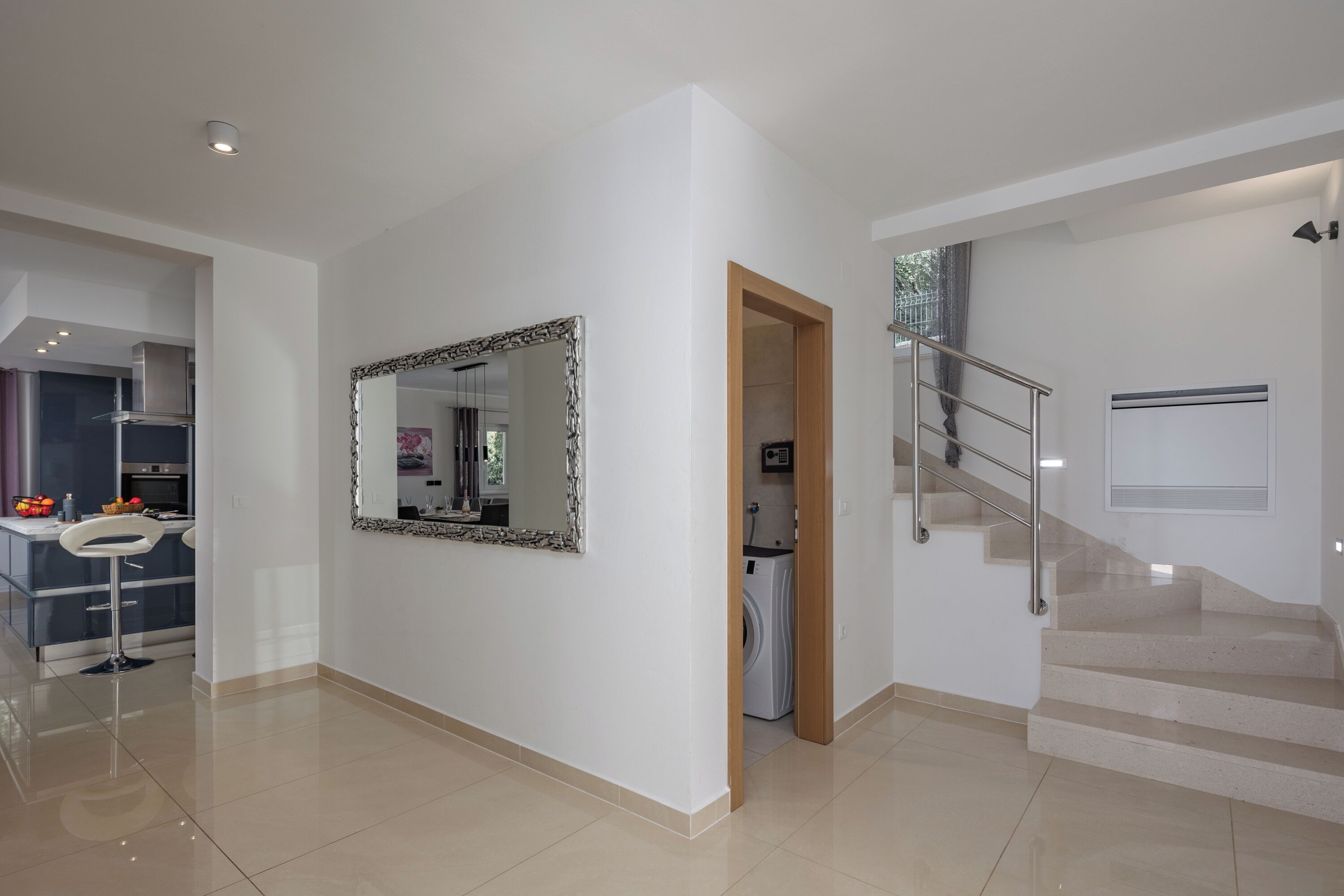 A modern interior with a kitchen, a large mirror, a staircase, and a laundry area.