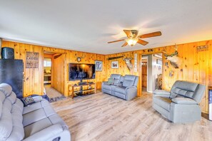 A cozy living room with a television, two gray sofas, a ceiling fan, and wooden walls with mounted animal heads. - Hunt, Fish & Hike: Home w/ Deck in Encampment (Encampment)