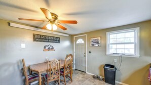 A dining area with a wooden table and chairs, a ceiling fan, a wall-mounted sign, a door, a window, and a trash can. - Hunt, Fish & Hike: Home w/ Deck in Encampment (Encampment)
