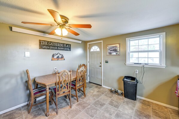 A dining area with a wooden table and chairs, a ceiling fan, a wall-mounted sign, and a window with a view. - Hunt, Fish & Hike: Home w/ Deck in Encampment (Encampment)
