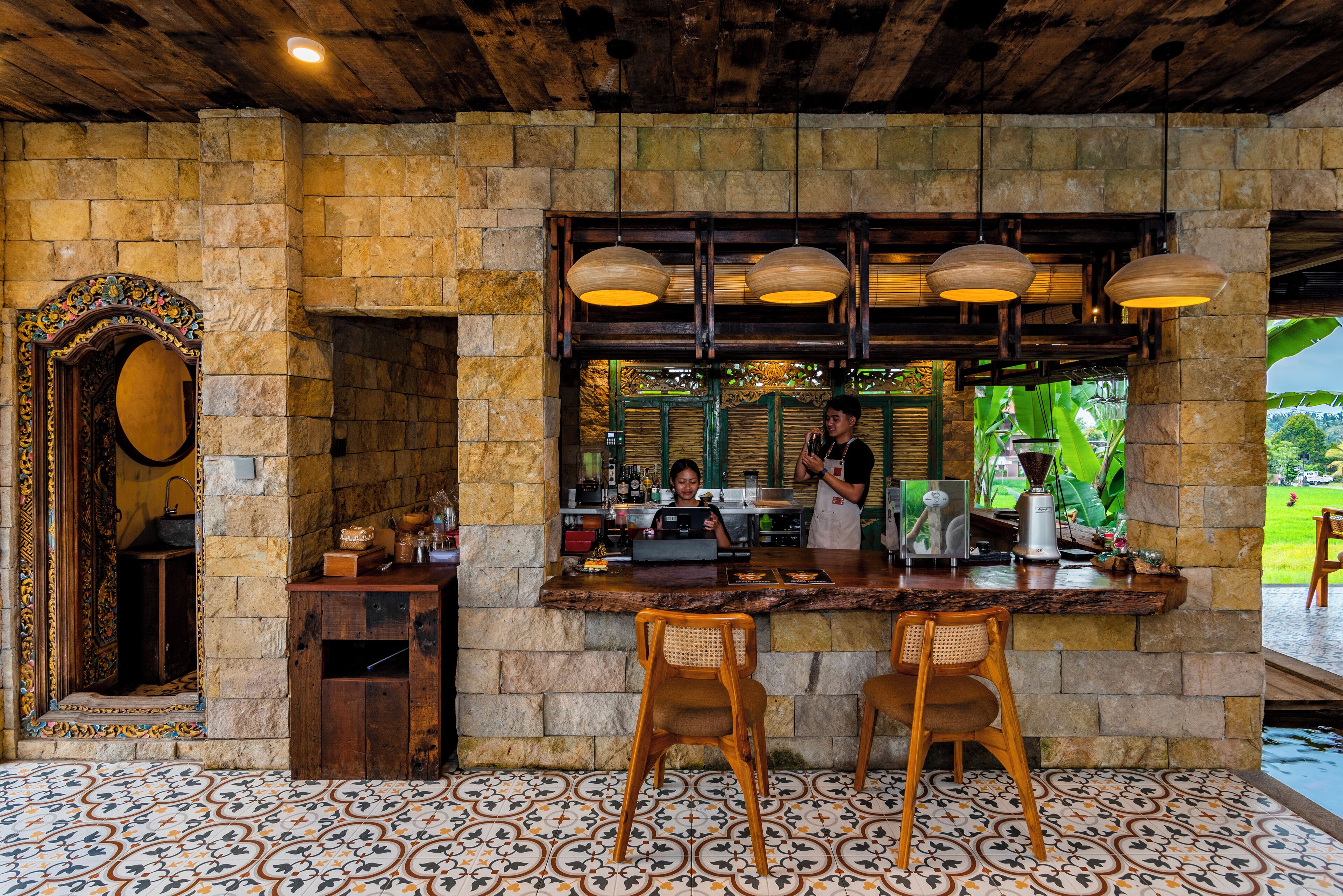A rustic bar area with stone walls, wooden ceiling, and patterned floor tiles.