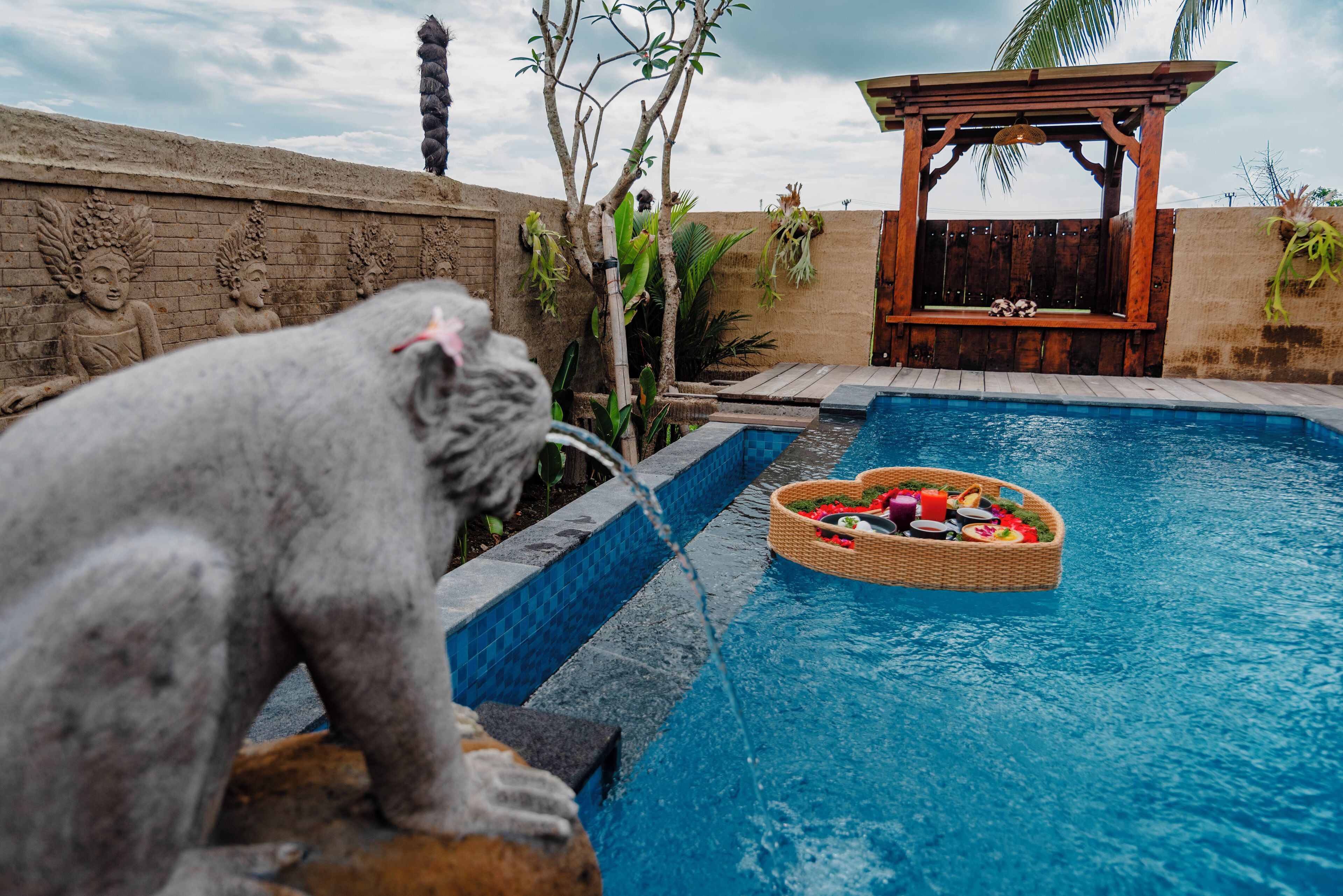 A pool area with a statue, a wooden pergola, and a wicker basket with food items.