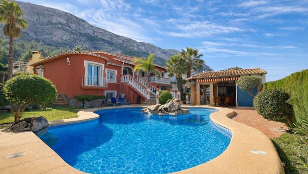 Una piscina con montagne sullo sfondo, un edificio rosso con una scalinata e un piccolo padiglione.