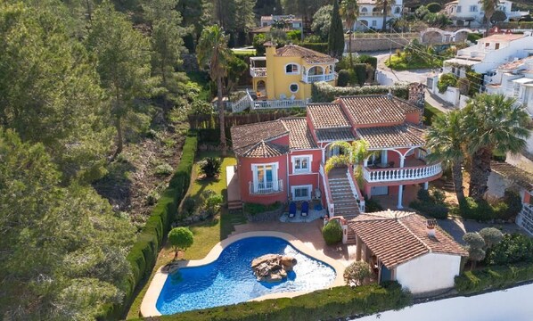 A large house with a swimming pool, surrounded by lush greenery and palm trees.