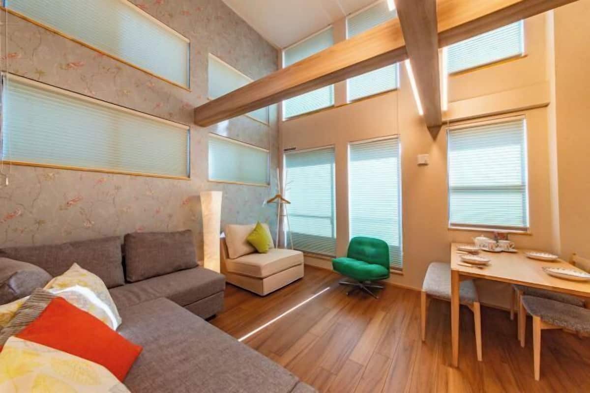 A modern living room with a sofa, a small table, a green chair, and a dining table.