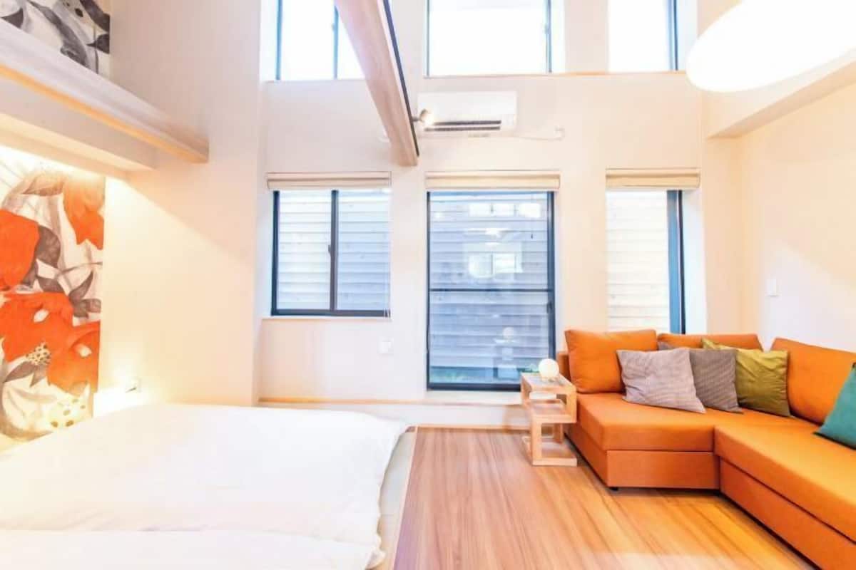 A modern hotel room with a bed, a sofa, a small table, and large windows.