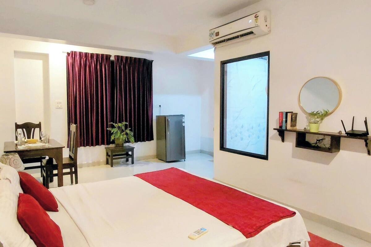 A hotel room with a bed, a desk, a chair, a TV, a mirror, and a plant.
