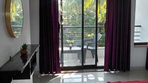 Quarto de hotel com cama, tapete vermelho, televisão sobre suporte e varanda com cortinas.