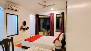 Quarto de hotel com cama, cadeira, mesa, espelho, janela e ventoinha no teto.