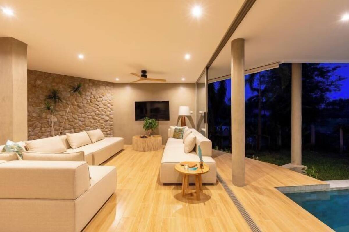 A modern living room with a stone wall, a flat-screen TV, and a pool area.