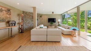 A modern living room with a sectional sofa, a flat-screen TV, and a large window offering a view of greenery. - Carbana Lodge, 2 Bedrooms - Eco Lodge, Koh Samui (Koh Samui)