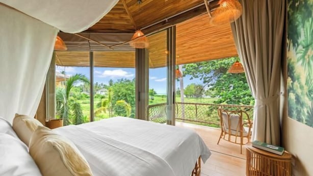 A bedroom with a large bed, a view of greenery, and a balcony with wicker furniture. - Carbana Lodge, 2 Bedrooms - Eco Lodge, Koh Samui (Koh Samui)