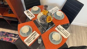 Ein runder Esstisch mit vier Stühlen, jeder mit einem blauen Teller und einer weißen Serviette. Der Tisch ist gedeckt, mit Besteck und einem Blumenarrangement in der Mitte.