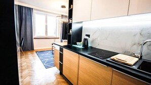 A modern kitchen with wooden cabinets, a black countertop, and a marble backsplash. - Nowolipki Studio, City Center Skyline View, WarsawStay (Warsaw)