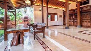 A spacious indoor area with a wooden bench and table, a tiled floor, and a traditional wooden door. - Joglo Wardani (Ngaglik)