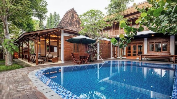 A swimming pool with a tiled edge, surrounded by wooden deck and lounge chairs. - Joglo Wardani (Ngaglik)