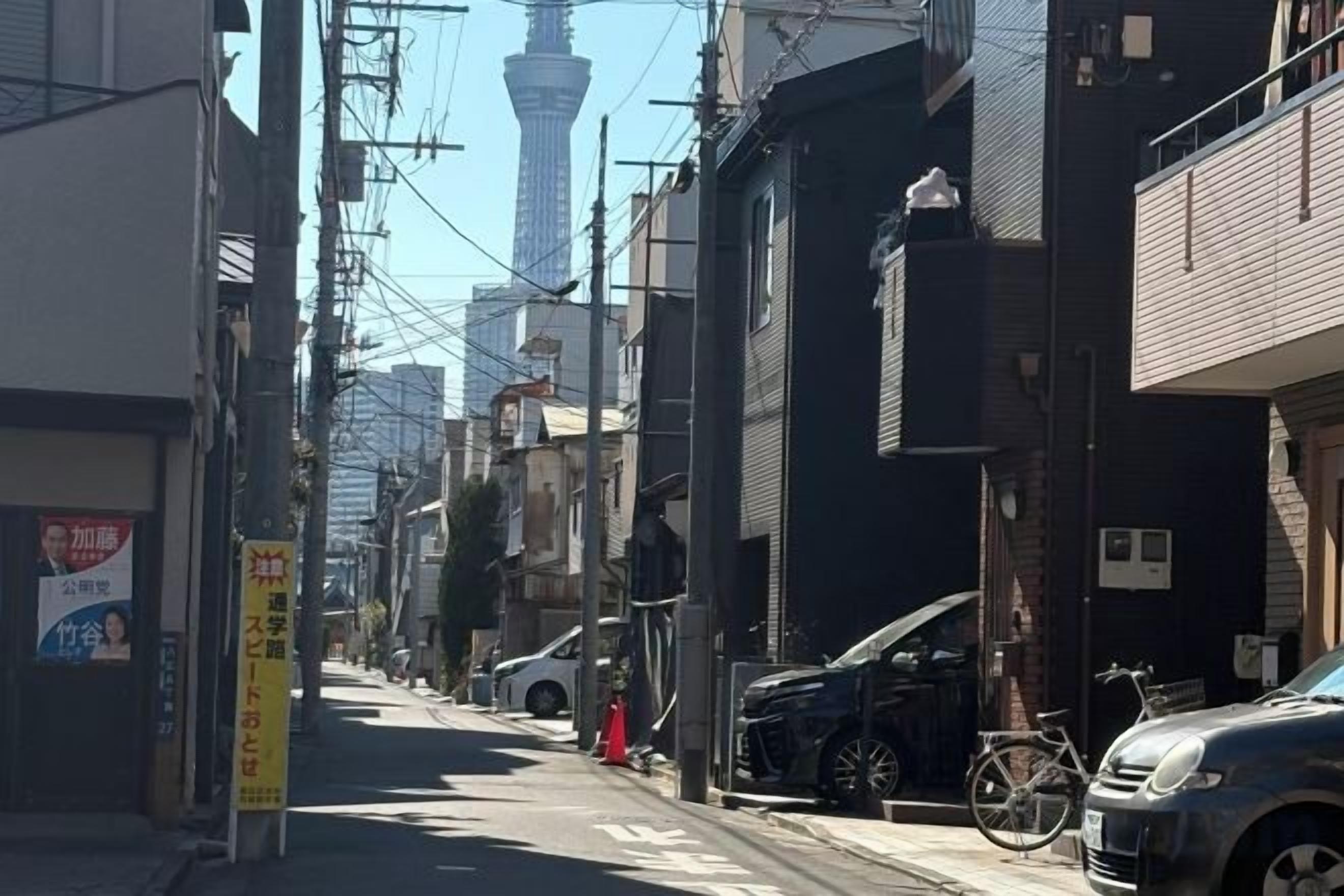 A narrow urban street with buildings, a bicycle, and a car parked on the side.