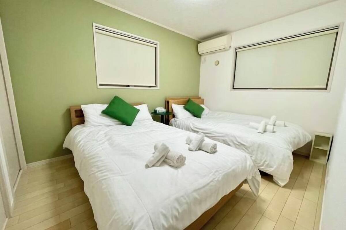 A hotel room with two beds, green pillows, white bedding, and towels.