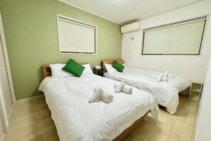 A hotel room with two beds, green pillows, white bedding, and towels. - Skytree Urban House (Tokyo)